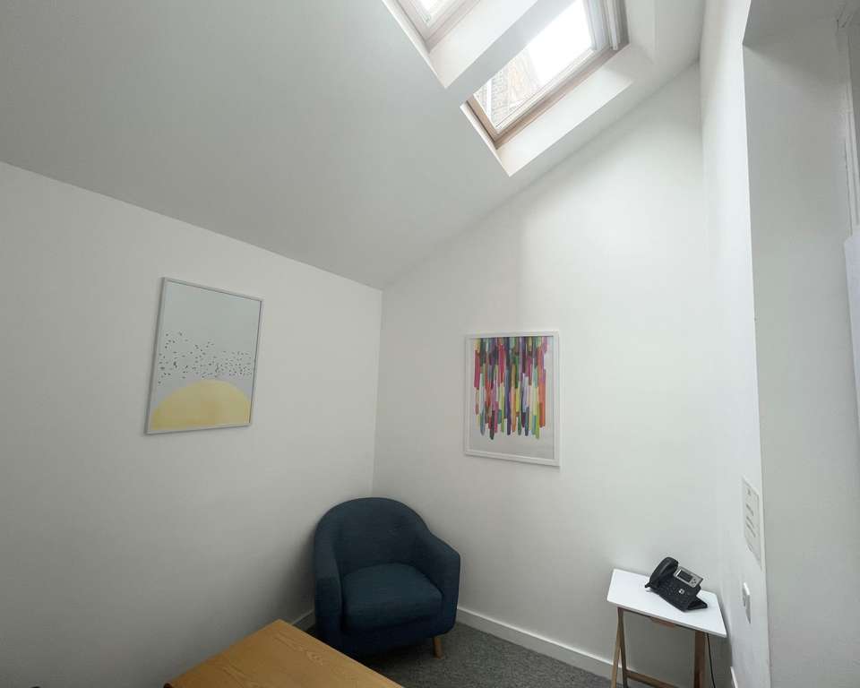 a photo of a small meeting room with two arm chairs and a coffee table, with white walls, a skylight and minimalist but colourful art on the walls