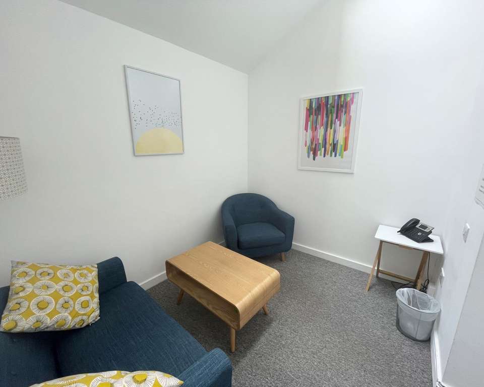 a photo of a small meeting room with two arm chairs and a coffee table, with white walls and minimalist but colourful art on the walls