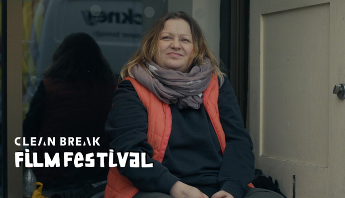 a still from Sandwiches. A woman sits on the ground on a street, she appears to be homeless