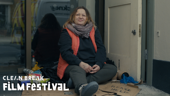 a still from Sandwiches. A woman sits on the ground on a street, she appears to be homeless