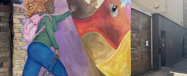 a mural of a woman walking towards colourful mountains