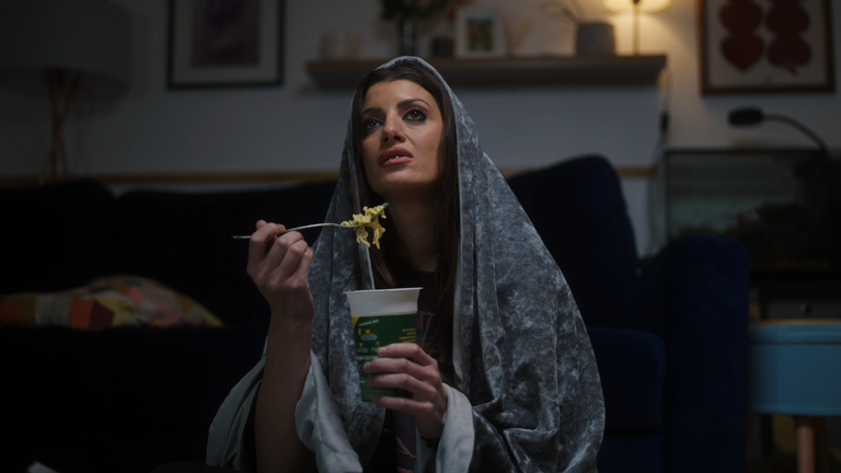 Natasha eating a pot noodle, wrapped in a blanket