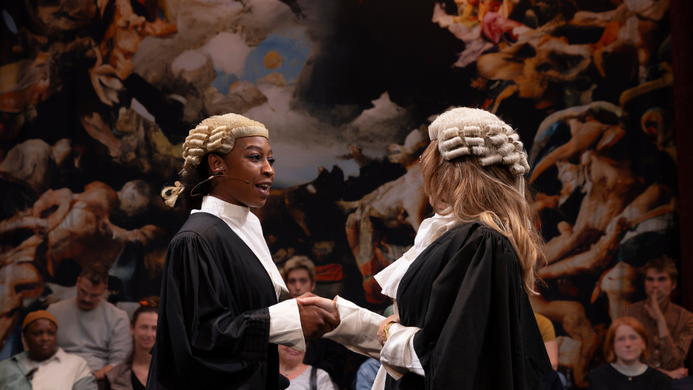 two women wearing judges or barristers wigs and gowns, there is a jury in the background