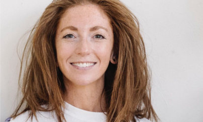 a head shot of Eva Sampson looking and smiling at the camera, she has red hair round her shoulders.