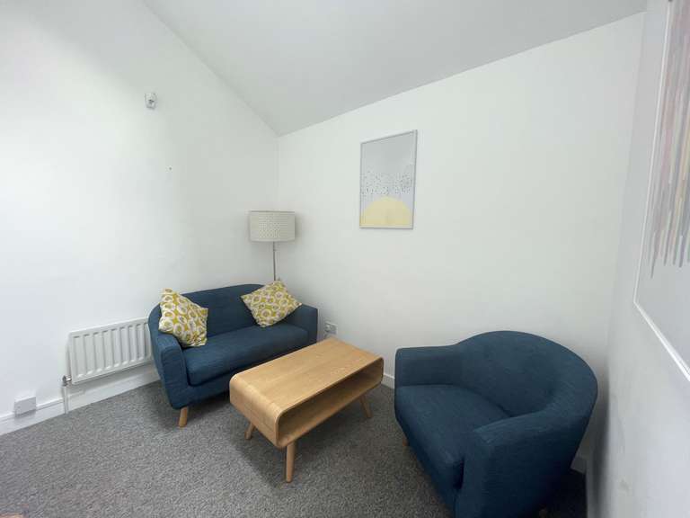 a photo of a small meeting room with two arm chairs and a coffee table, with white walls