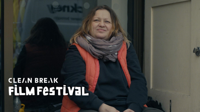 a still from Sandwiches. A woman sits on the ground on a street, she appears to be homeless