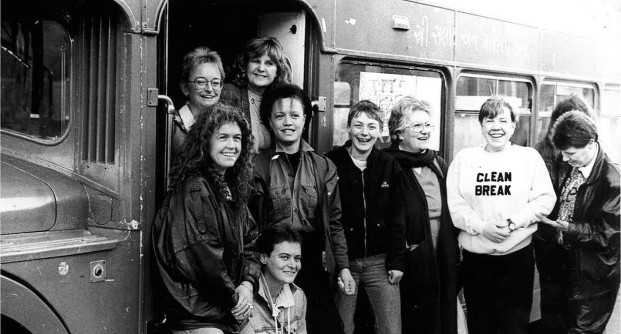 A black and white photo from the 1980s shows 8 Clean Break Members stand smiling in front of the company van with the Lord Mayor. They're all wearing casual clothes & one wearing a Clean Break jumper.