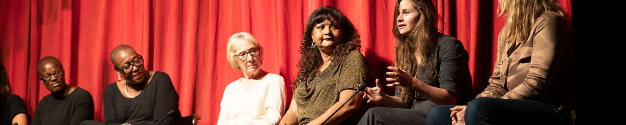clean break writers sat on a stage in front on a red curtain