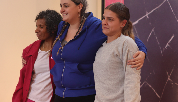a photo of the cast of catch taking bows at the end of a performance. they are smiling and have their arms around each other