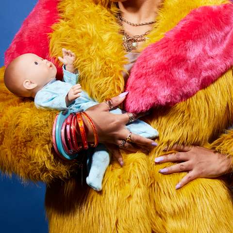 A woman's torso, wearing a brightly coloured fur coat, holding and baby doll