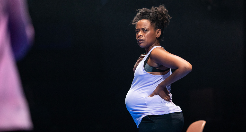 A pregnant woman stands with her hand on her hip looking with concern at an unseen person.