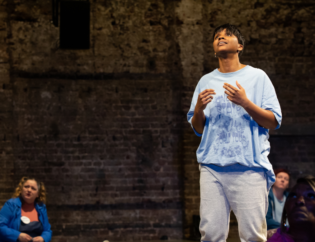 A photo from More Than We Can Bear, a woman is standing on stage looking towards the ceiling.