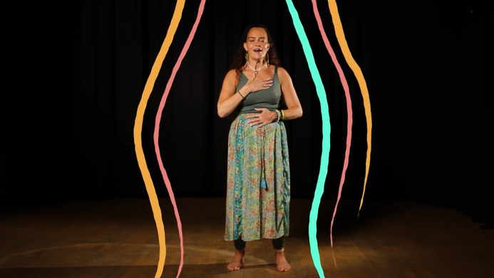 Michelle Hamilton standing in a studio, with illustrations of colourful lines around her, she has one hand on her heart and one hand on her stomach