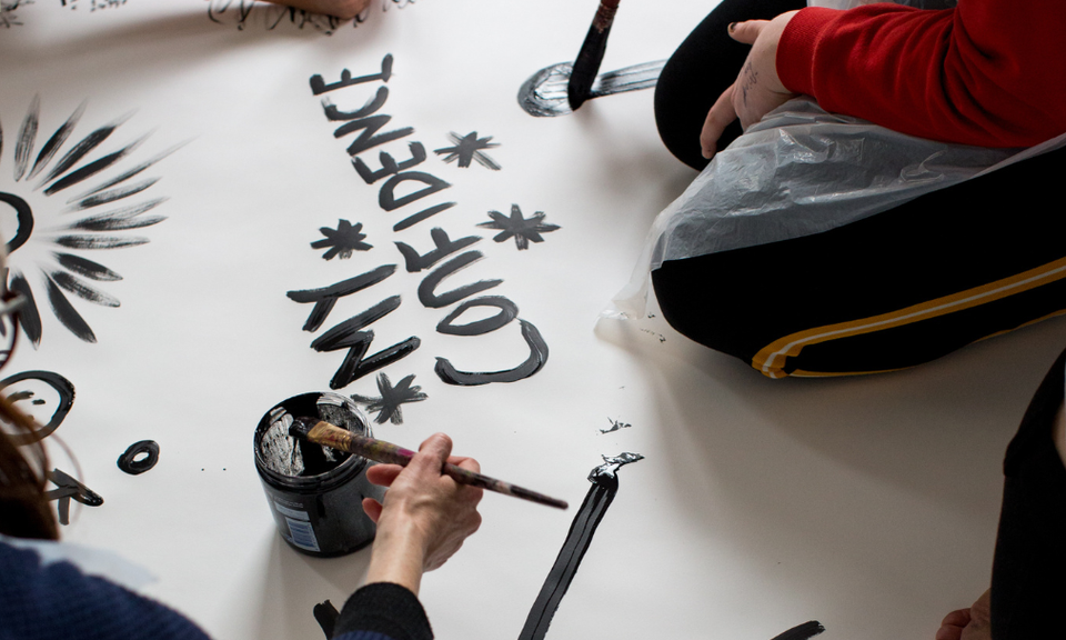 a photo of women kneeling on the floor painting the words 'my confidence' on a piece of paper
