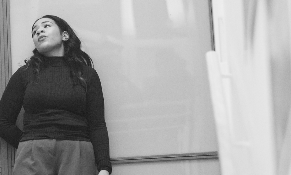 A black and white photo of a woman at the top of a staircase staring out of the window.