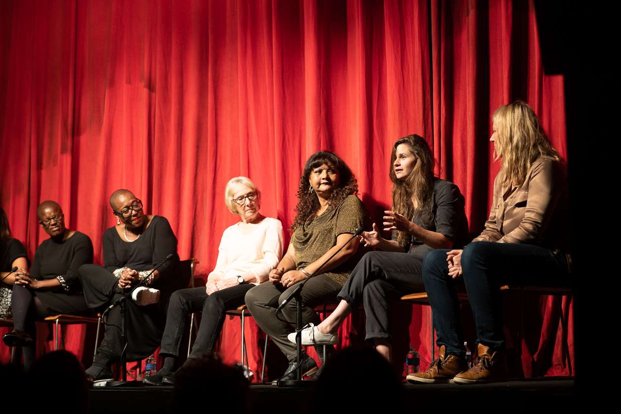 clean break writers sat on a stage in front on a red curtain