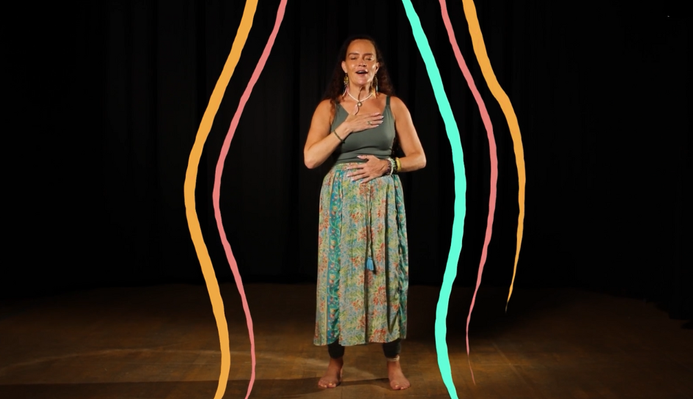 Michelle Hamilton standing in a studio, with illustrations of colourful lines around her, she has one hand on her heart and one hand on her stomach