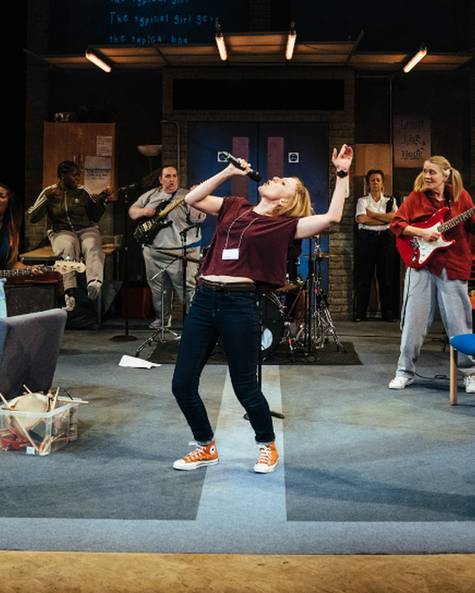 a photo of a group of women on stage in the play Typical Girls, they are a band performing