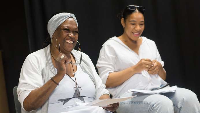 a photo of two women sitting on chairs and holding scripts, they are smiling