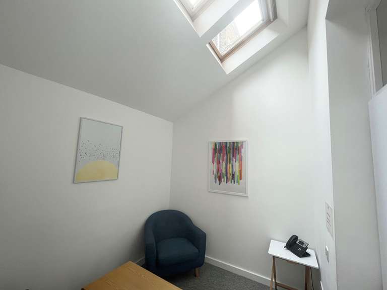 a photo of a small meeting room with two arm chairs and a coffee table, with white walls, a skylight and minimalist but colourful art on the walls