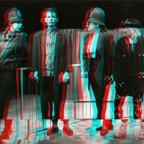 a black and white photo with a distorted affect over the top of a Clean Break production from the 80s, there are four women on stage, three are in police hats with pig noses on.