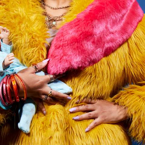 A woman's torso, wearing a brightly coloured fur coat, holding and baby doll