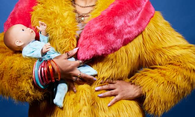A photo of a woman wearing a bright yellow and pink fur jacket holding a baby doll, you can't see her face
