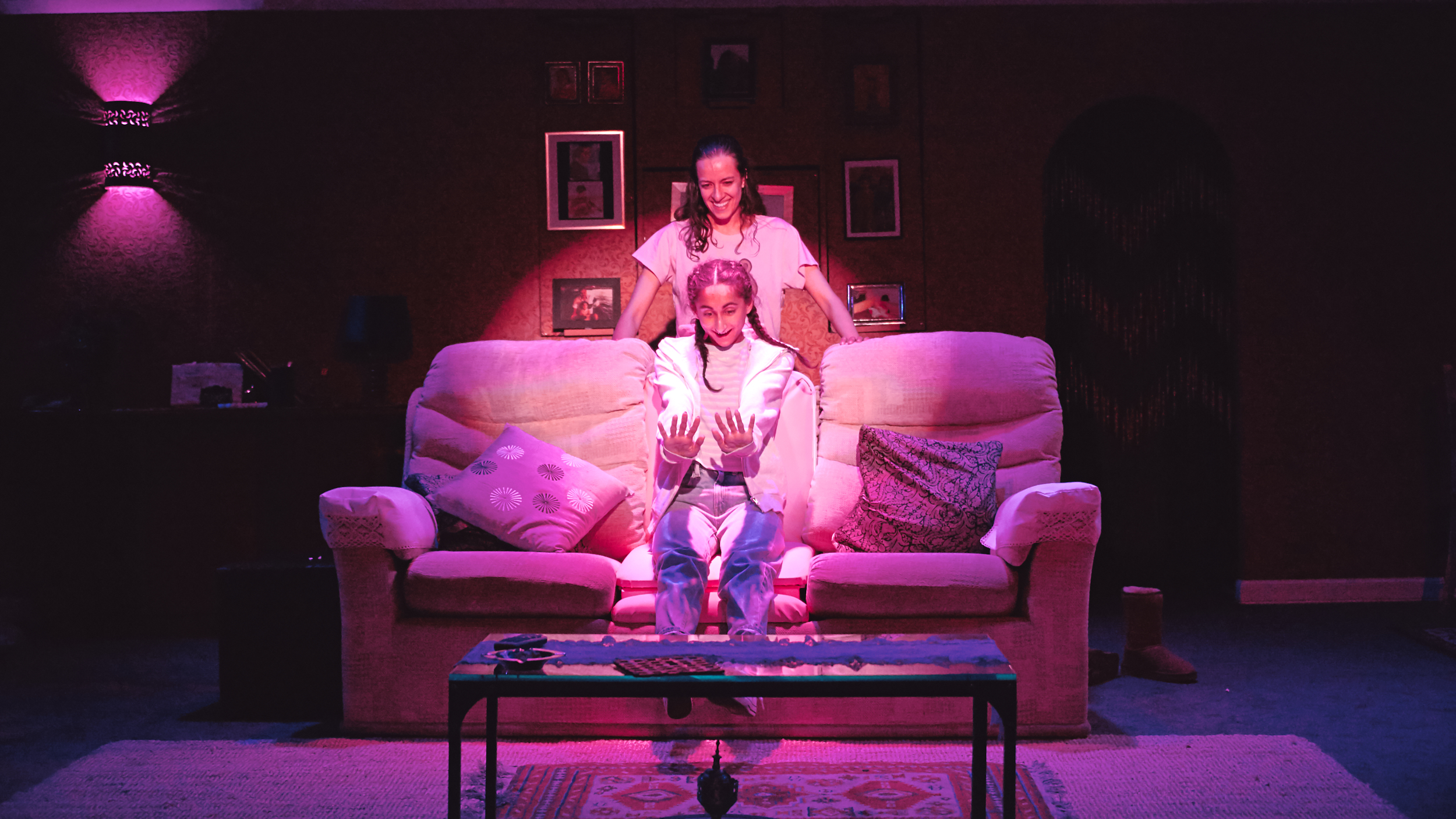 a photo of the set of Favour, Leila is sitting on the sofa which has turned into a salon chair, there is pink lighting and she is looking at her nails
