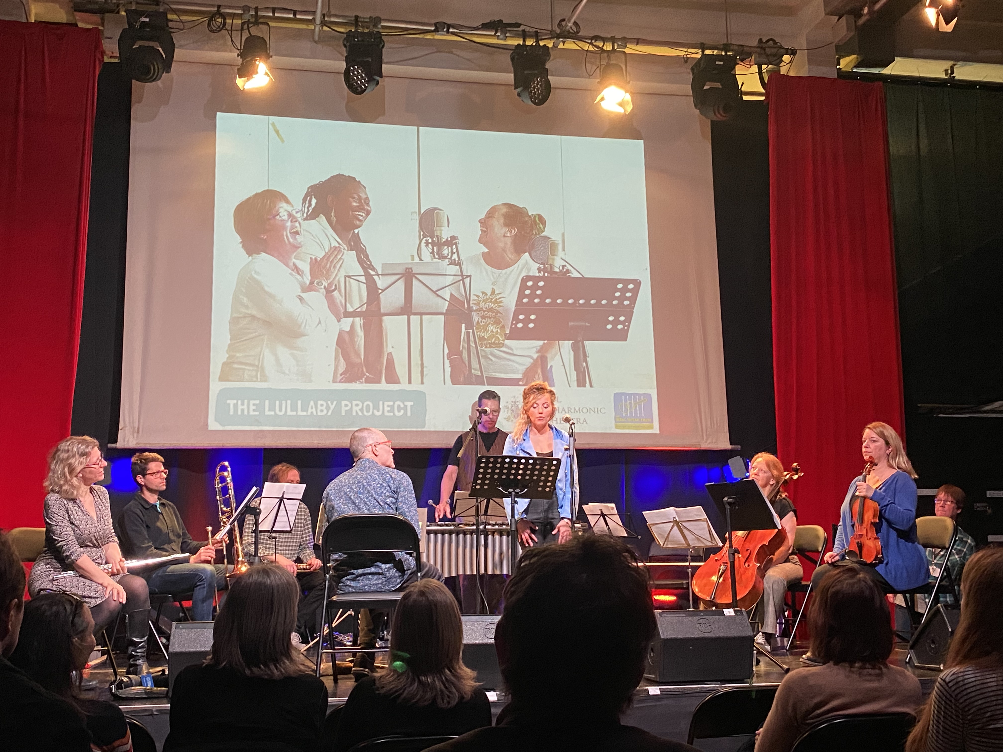 Clean Break member Michaela is standing on stage with musicians from the Royal Philharmonic Orchestra, preparing to sing.