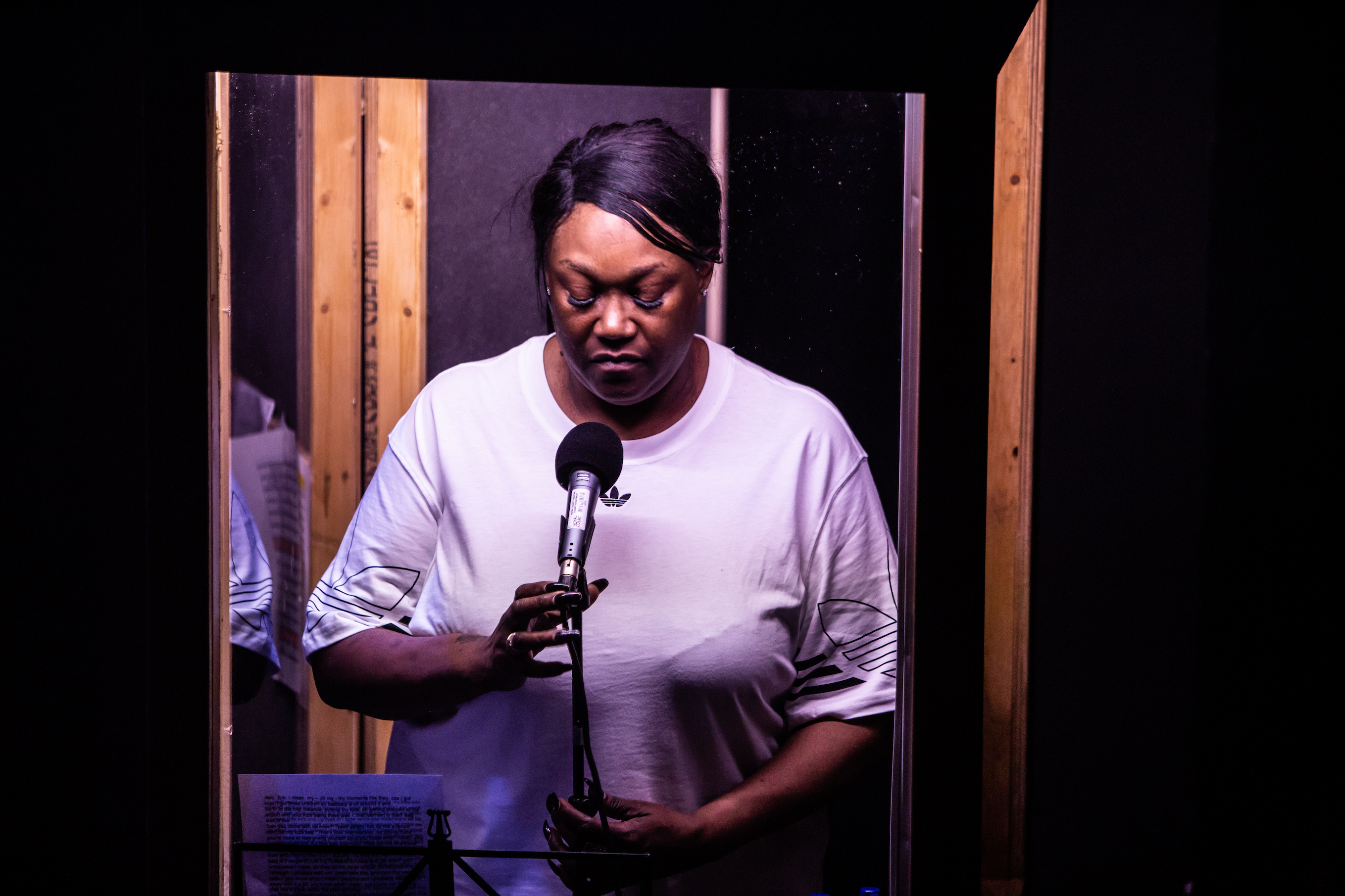 A photo of Jennifer Joseph speaking into a microphone standing in a perspex box